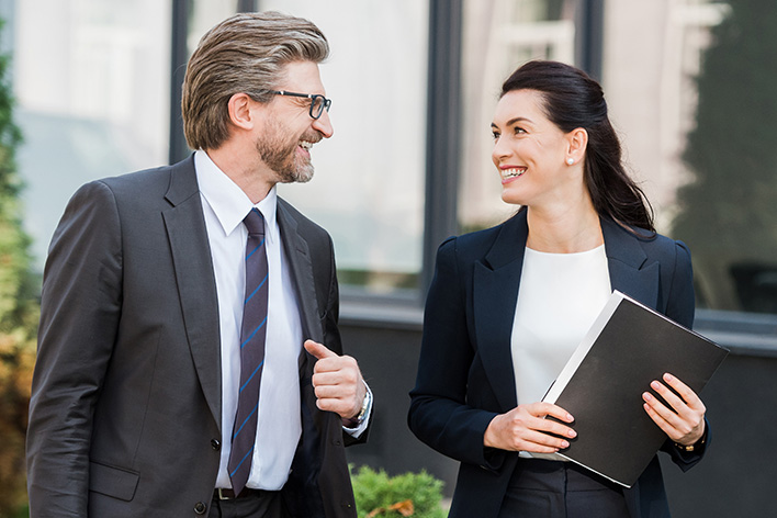 Photo of a man and a businesswoman in suits smiling outdoors
