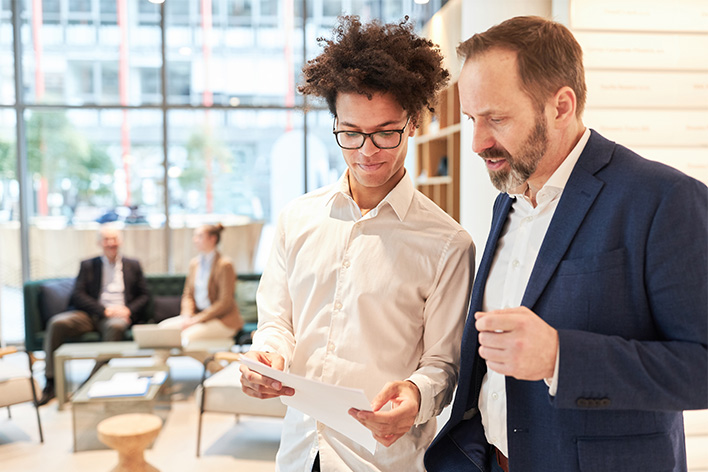 photo of two men talking business with documents in hand in a lobby